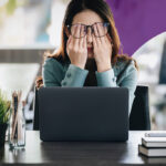 A tired accountant working on manual accounting tasks at a desk with a computer and piles of paper