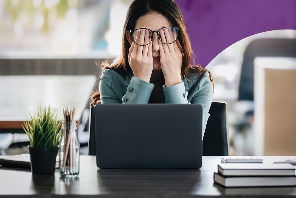 A tired accountant working on manual accounting tasks at a desk with a computer and piles of paper